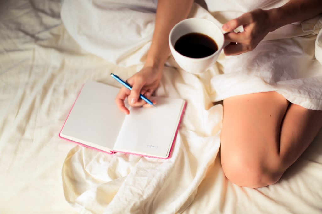 femme sur son lit buvant un café et écrivant son journal