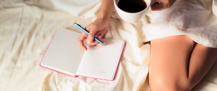 femme sur son lit buvant un café et écrivant son journal